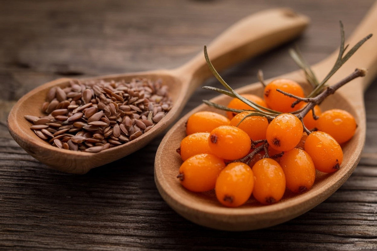 Two wooden spoons on a rustic dark wood surface, one filled with brown flaxseeds and the other holding a vibrant branch of orange sea buckthorn berries.