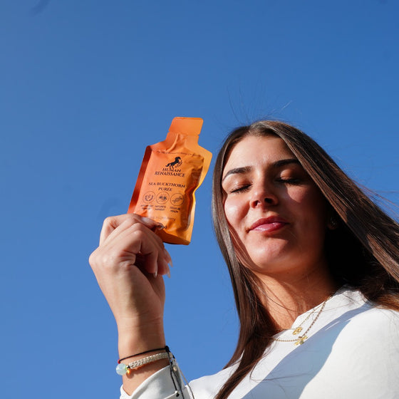 A woman holding a Human Renaissance sea buckthorn puree pouch against a clear sky